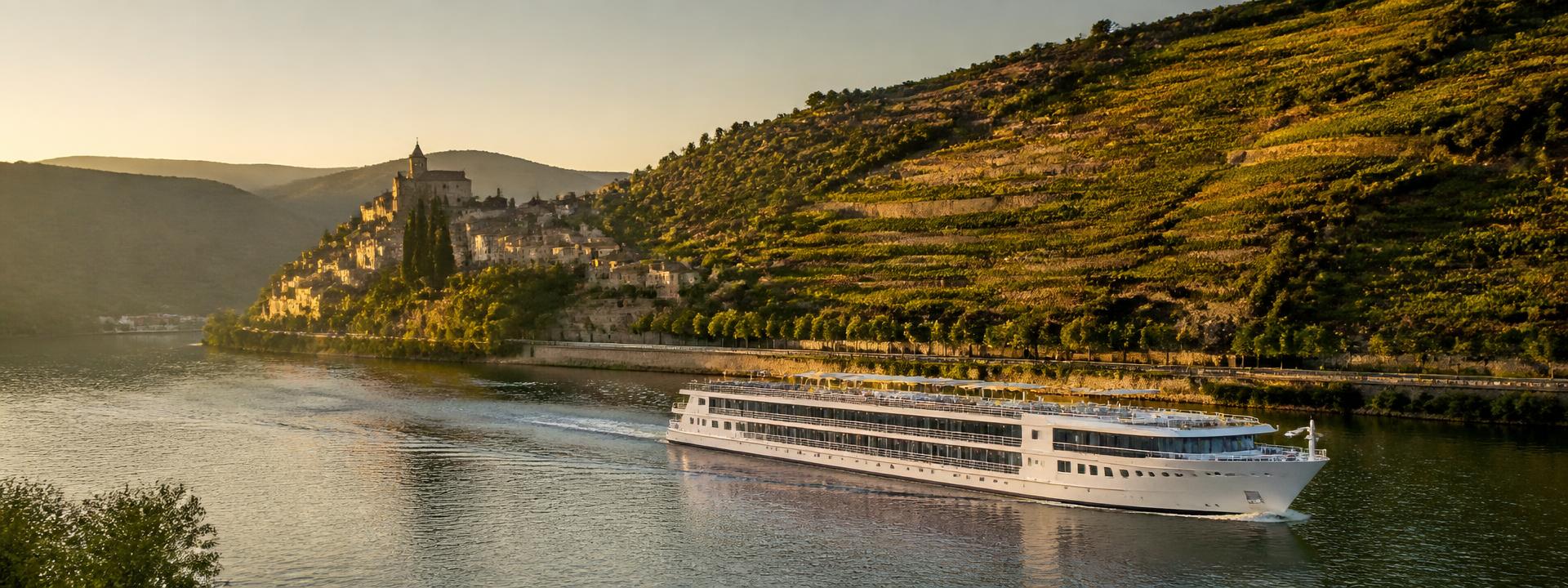 A small river cruise ship passing terraced vineyards at golden hour